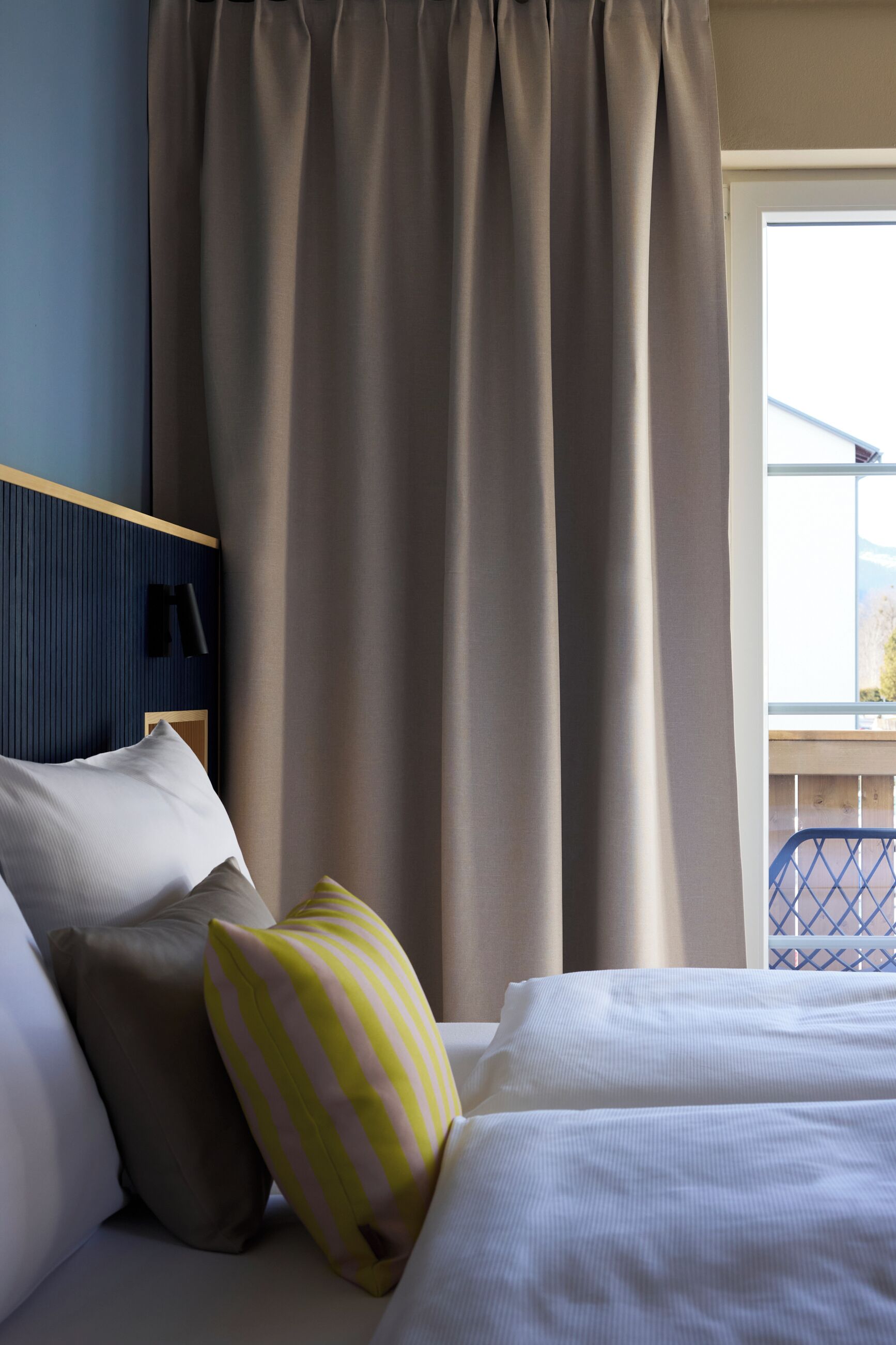 A hotel room with a bed, pillows, a headboard, and a window with curtains.