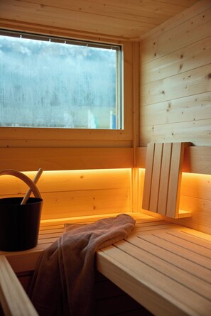 A sauna with wooden benches, a window, and a towel. - Hotel UND smart alpine stay (Schladming)