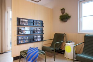 A waiting area with a wooden wall, a bulletin board with magazines, and two green chairs.
