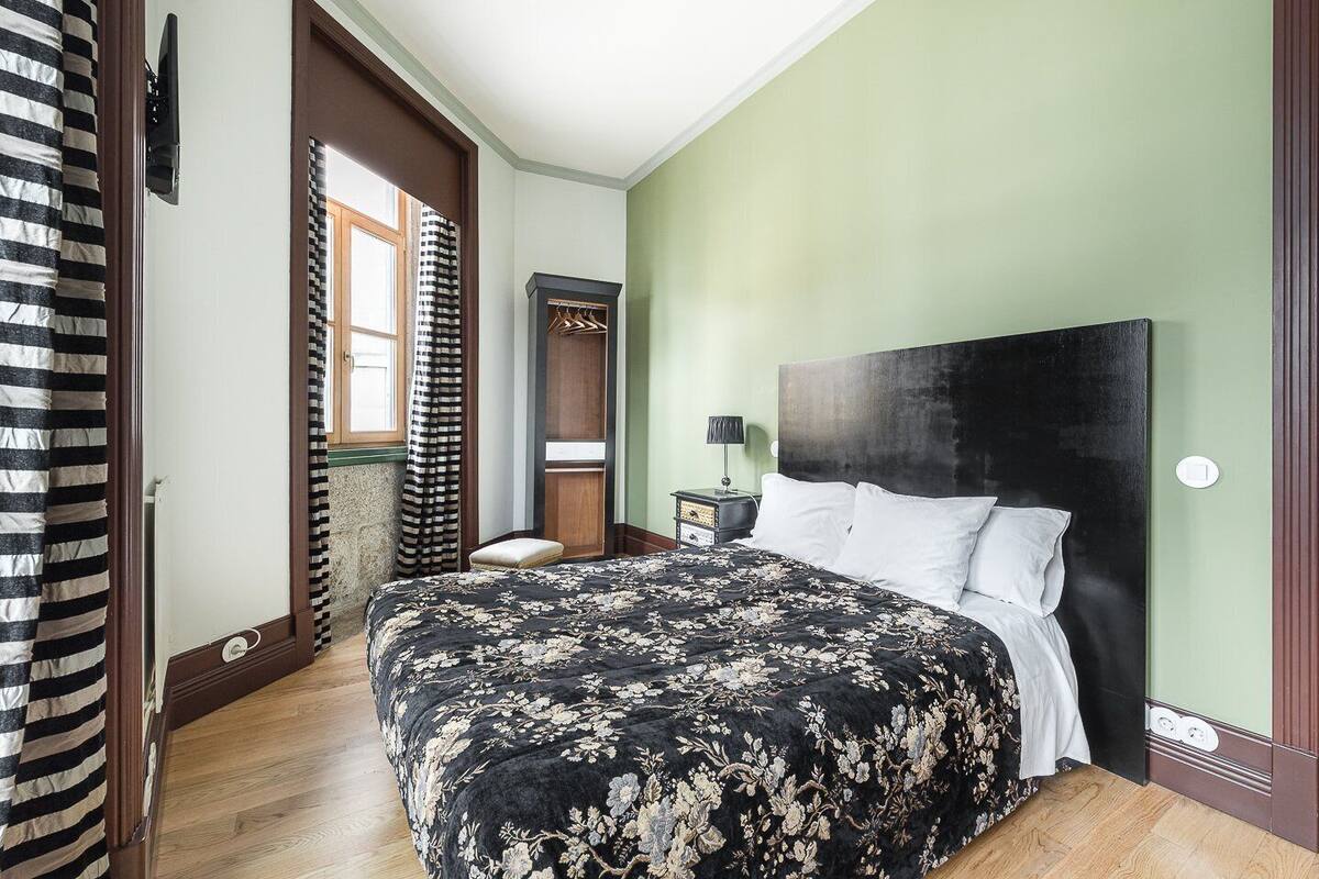 A bedroom with a large bed, a nightstand, a dresser, and a window with curtains.