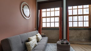 Un salon moderne avec un canapé gris, des coussins à motifs, une horloge ronde et une petite table sur laquelle se trouve une télécommande.