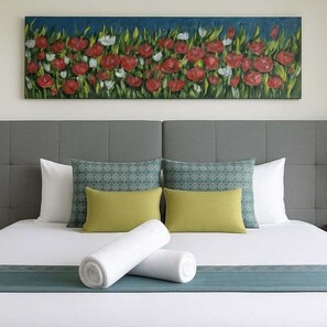Ein ordentlich bezogenes Bett mit grauem Kopfteil, zwei Kissen mit geometrischem Muster und ein aufgerolltes weißes Handtuch.