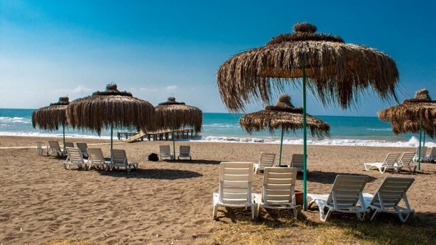 A beach with thatched umbrellas and white lounge chairs. - Doramar Resort Aqua Tatilkoyu (Erdemli)