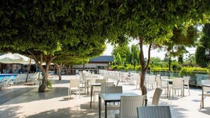 An outdoor seating area with tables and chairs, a pool, and a building in the background. - Doramar Resort Aqua Tatilkoyu (Erdemli)