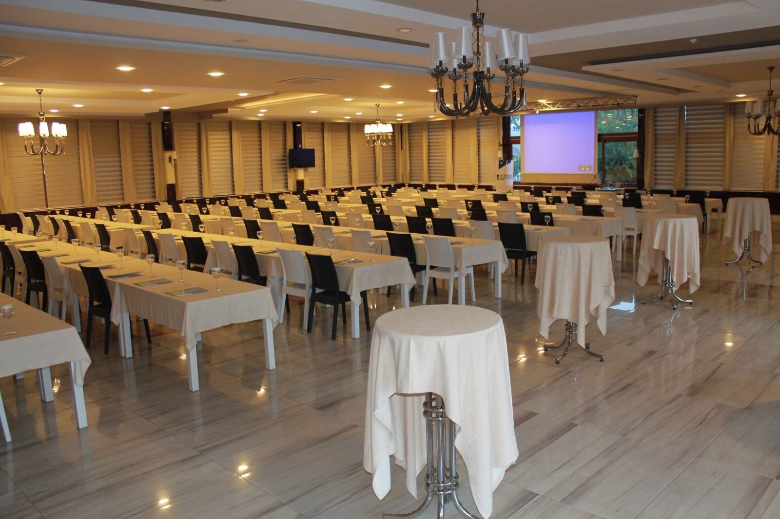 A conference room with rows of tables, chairs, and a large screen for presentations.