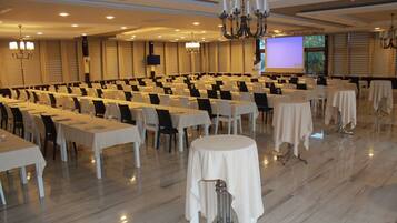 Un salón de conferencias con filas de mesas, sillas y una gran pantalla para presentaciones.