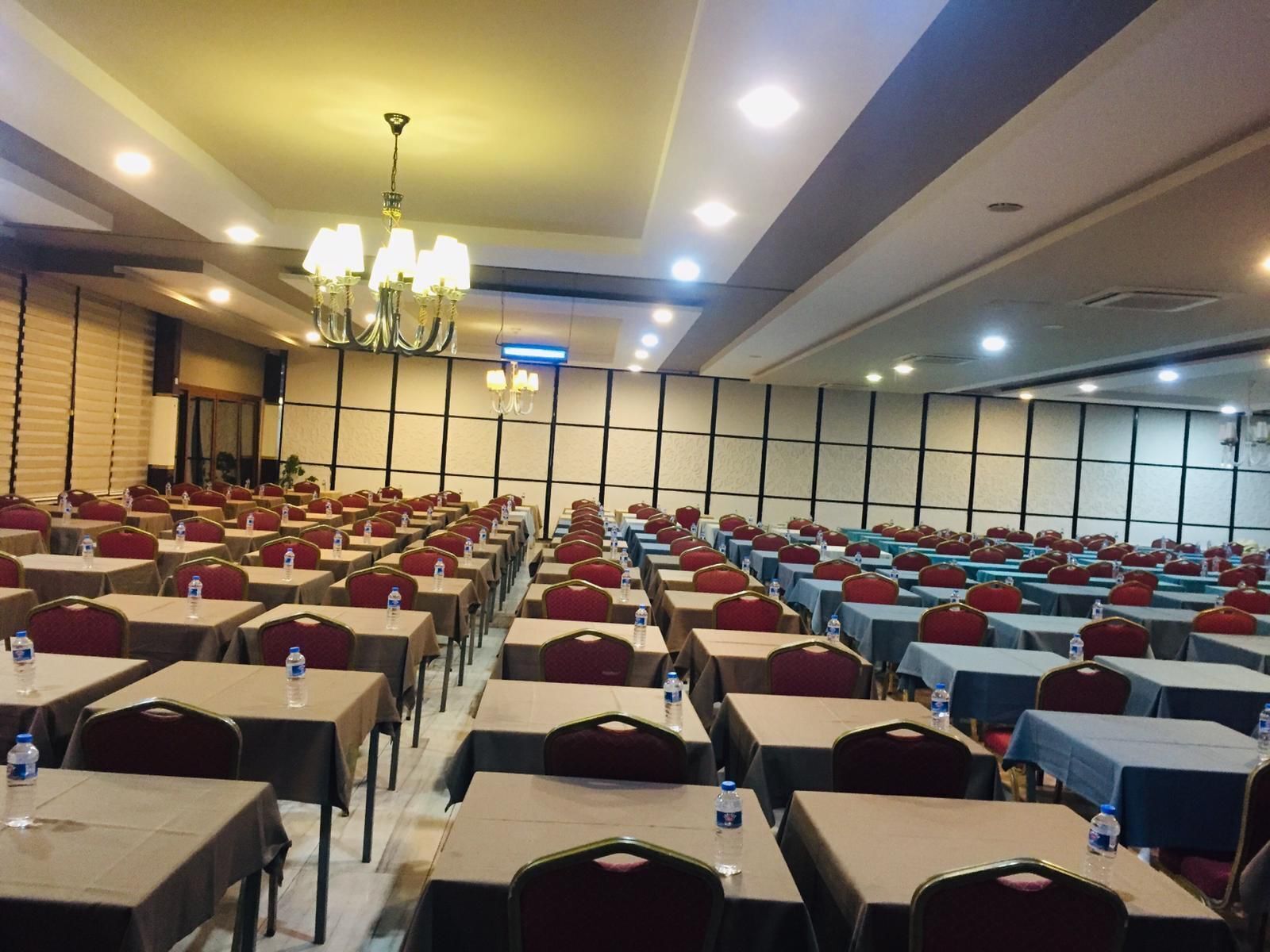 A conference room with rows of tables and chairs, equipped with water bottles, and a chandelier.