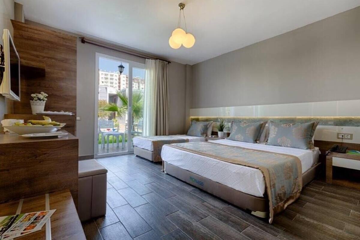 A hotel room with a large bed, a desk with a chair, a TV, and a balcony with a view of palm trees.