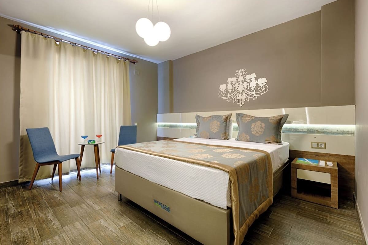 A hotel room with a large bed, a desk, a chair, and a chandelier.