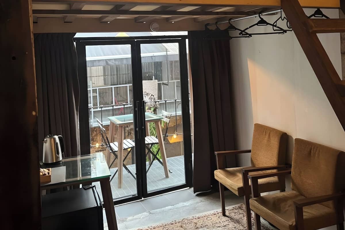 A loft-style room with a glass door leading to a patio, a small table with a kettle, and two chairs.