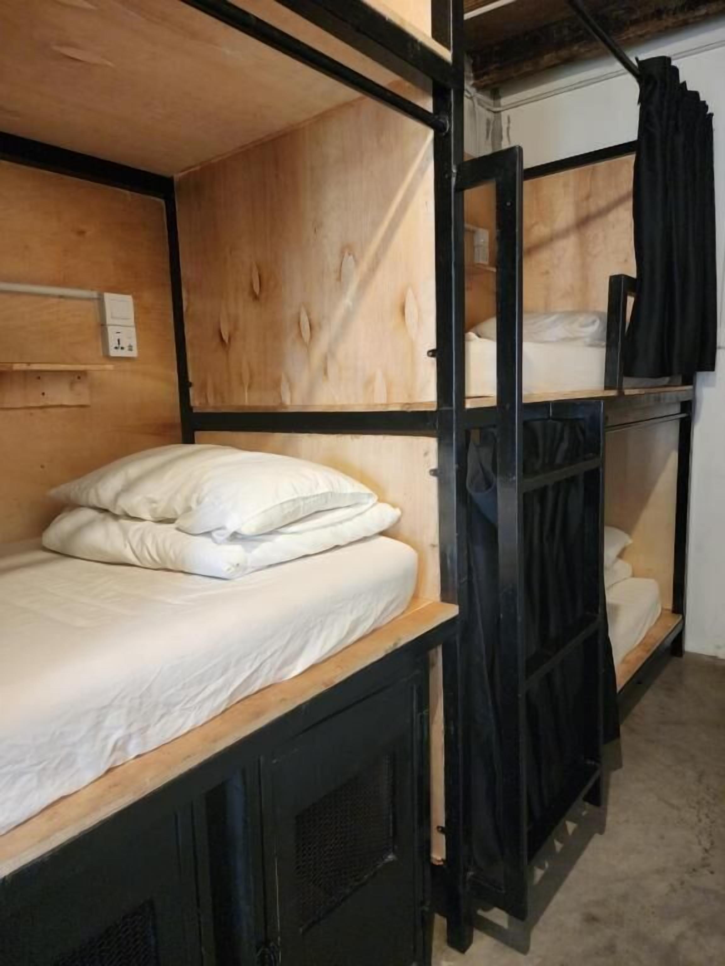 A bunk bed room with wooden headboards, a power outlet, and a black curtain.