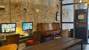 A rustic bar area with wooden furniture, a piano, and two monitors displaying video games. - Mingle Highstreet (Kuala Lumpur)