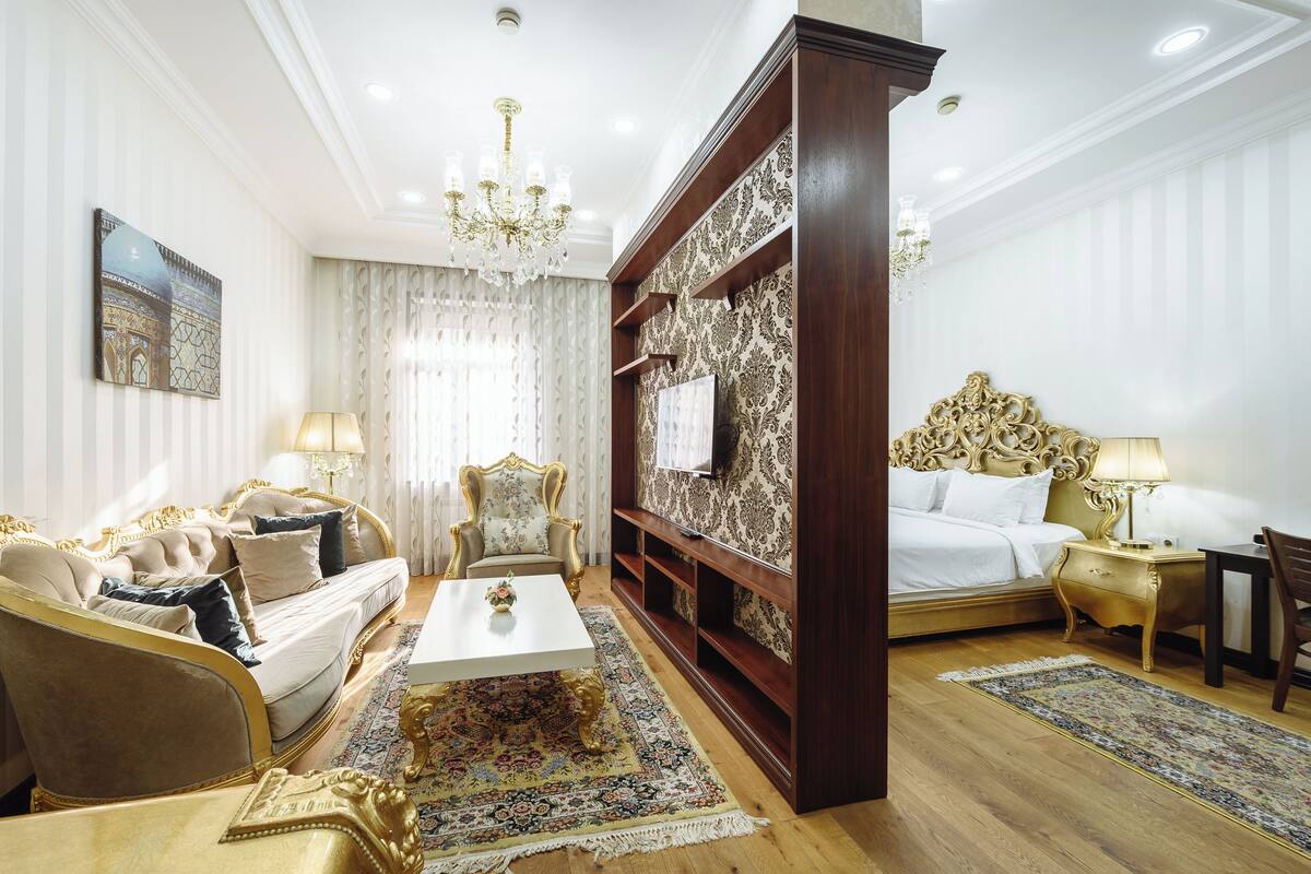 Une chambre luxueuse comprenant un canapé, un fauteuil, un lit, une table de chevet et un lustre.