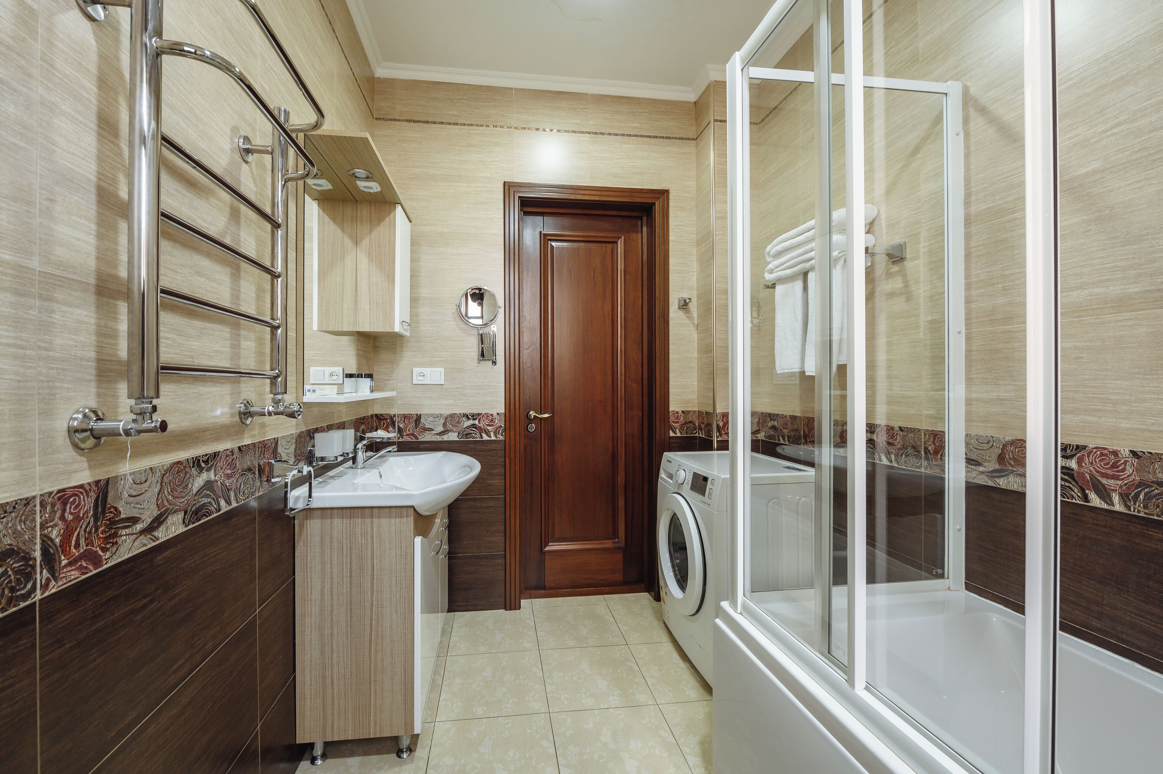 A compact bathroom with a sink, mirror, towel rack, and a glass-enclosed shower area.