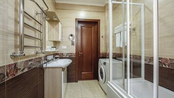 A compact bathroom with a sink, mirror, towel rack, and a glass-enclosed shower area.