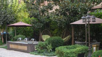 Ein Gartenbereich mit Wasserspiel, Sitzgelegenheiten und Sonnenschirmen.