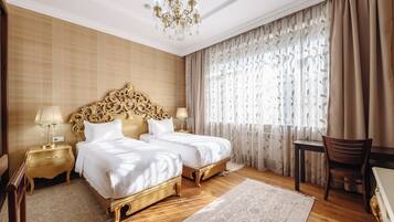 Habitación de hotel con dos camas, un candelabro, suelo de madera y un ventanal con cortinas.