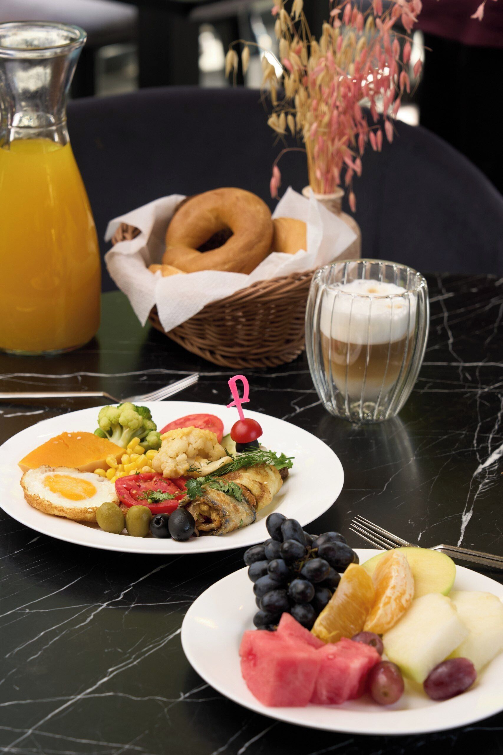 Un desayuno con platos de comida, un vaso de jugo y una taza de café sobre una mesa de mármol.