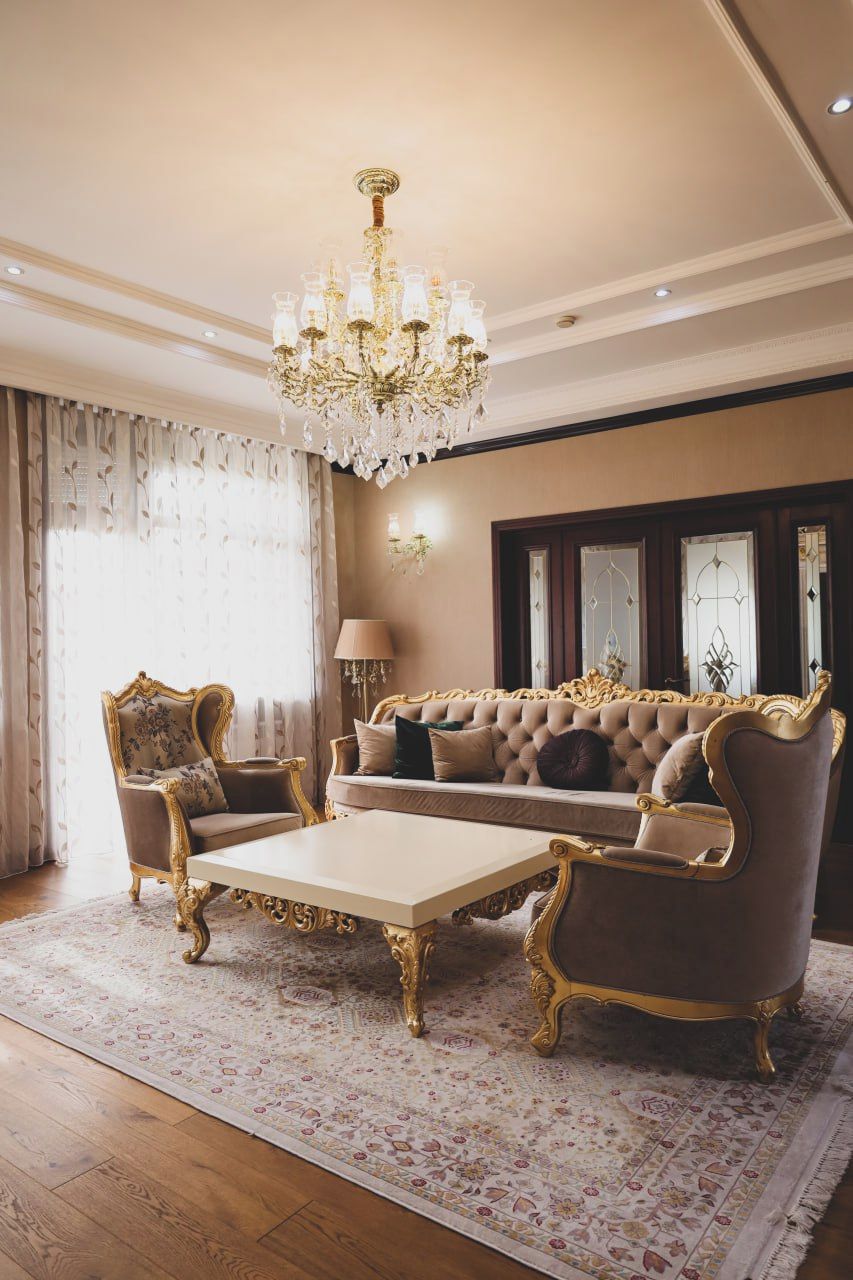Uma sala de estar luxuosa com um amplo sofá, poltronas ornamentadas, uma mesa de centro e um candelabro.