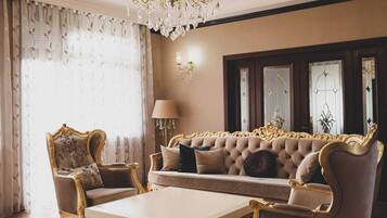 Uma sala de estar luxuosa com um amplo sofá, poltronas ornamentadas, uma mesa de centro e um candelabro.