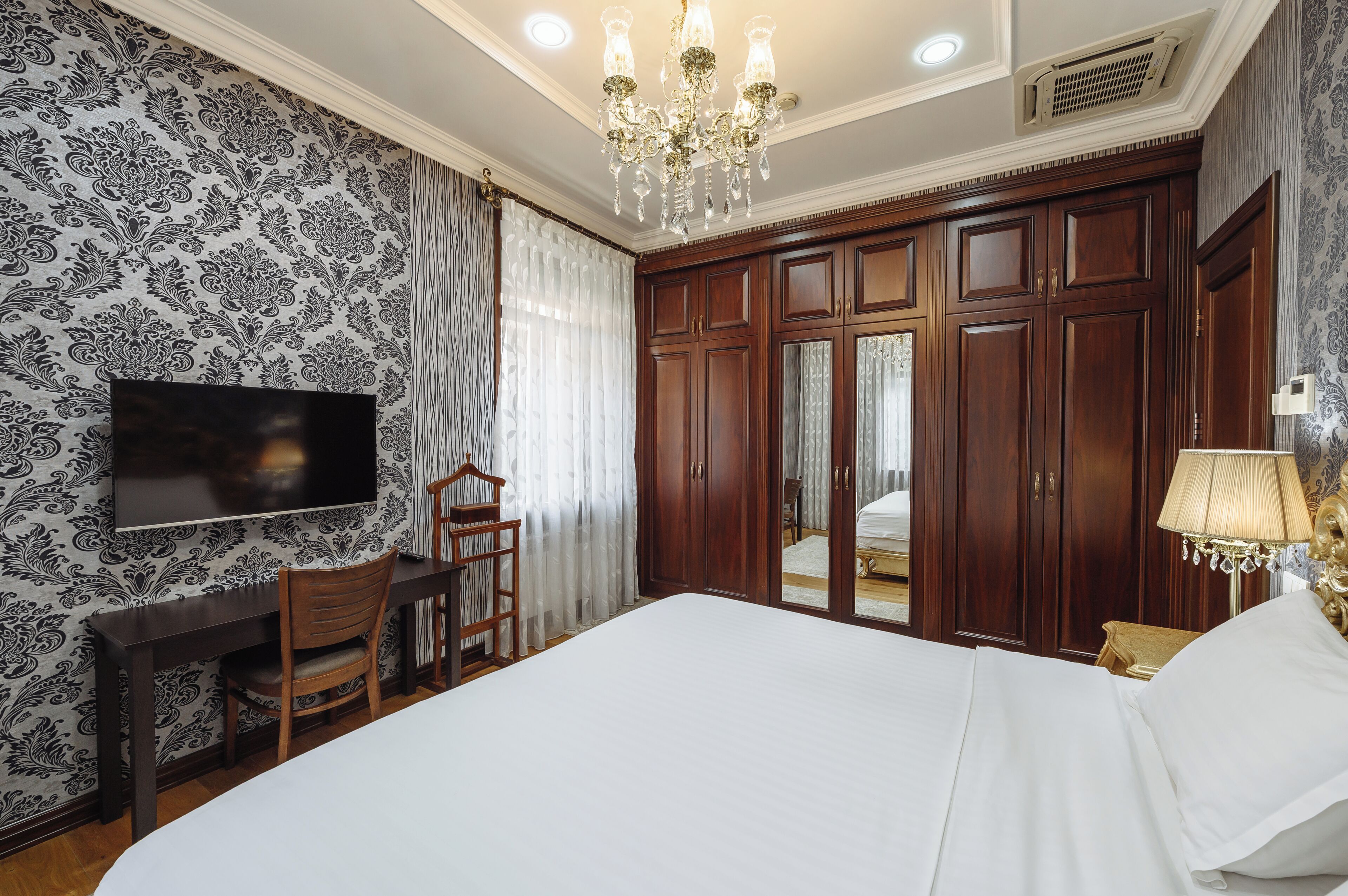 Quarto de hotel com uma cama grande, uma escrivaninha com cadeira, televisão e guarda-roupa.