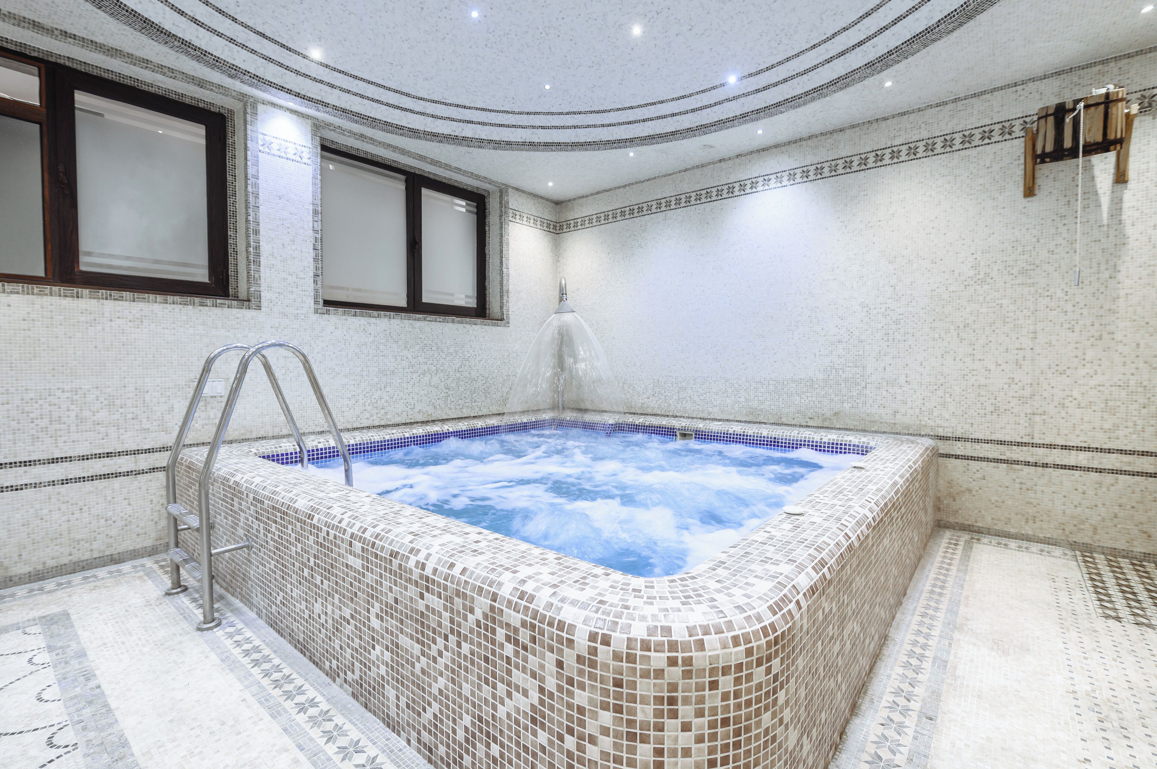 Une salle de bain moderne avec un jacuzzi orné de mosaïques, une douche à parois de verre et un tapis de bain en bois.