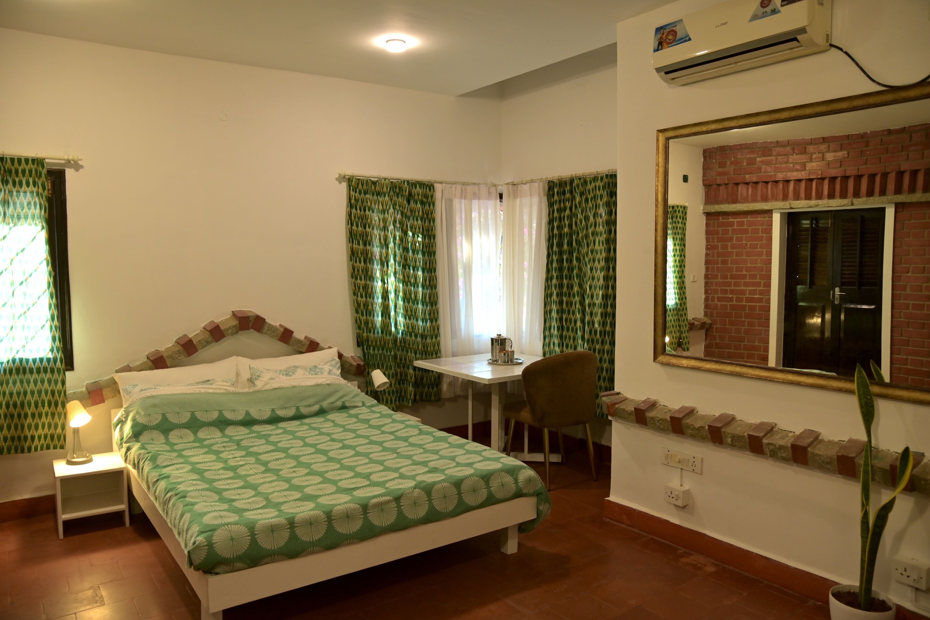A bedroom with a bed, a desk, a chair, a potted plant, and a window with curtains.