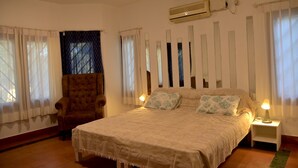 A bedroom with a bed, a chair, a nightstand, an air conditioner, and curtains. - Namma Ashram (Bengaluru)
