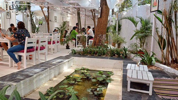 An indoor dining area with white tables and chairs, a small water feature, and various potted plants. - Namma Ashram (Bengaluru)
