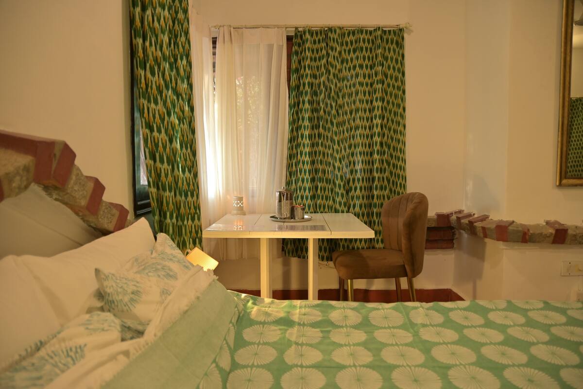 Um quarto com cama, uma mesa com cadeira e uma janela com cortinas.