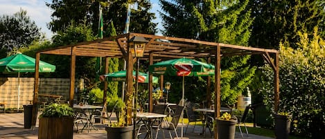 An outdoor patio area with tables and chairs, surrounded by potted plants and umbrellas.