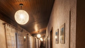 A hotel corridor with wooden panel ceilings, a long hallway with curtains, a table with plates and cups, and framed pictures on the walls.