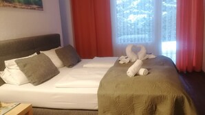 A bedroom with a bed, pillows, a blanket, a wooden table, and a painting on the wall.