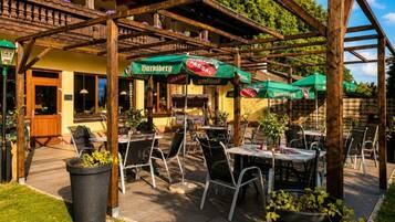 Een terras met tafels en stoelen, groene parasols en een houten pergola.