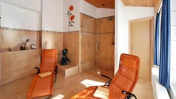 Une pièce avec deux fauteuils orange, un espace douche, une horloge et une porte.
