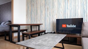 Un salon moderne avec un téléviseur à écran plat diffusant des vidéos de YouTube, une table basse en bois, un petit banc et un canapé.