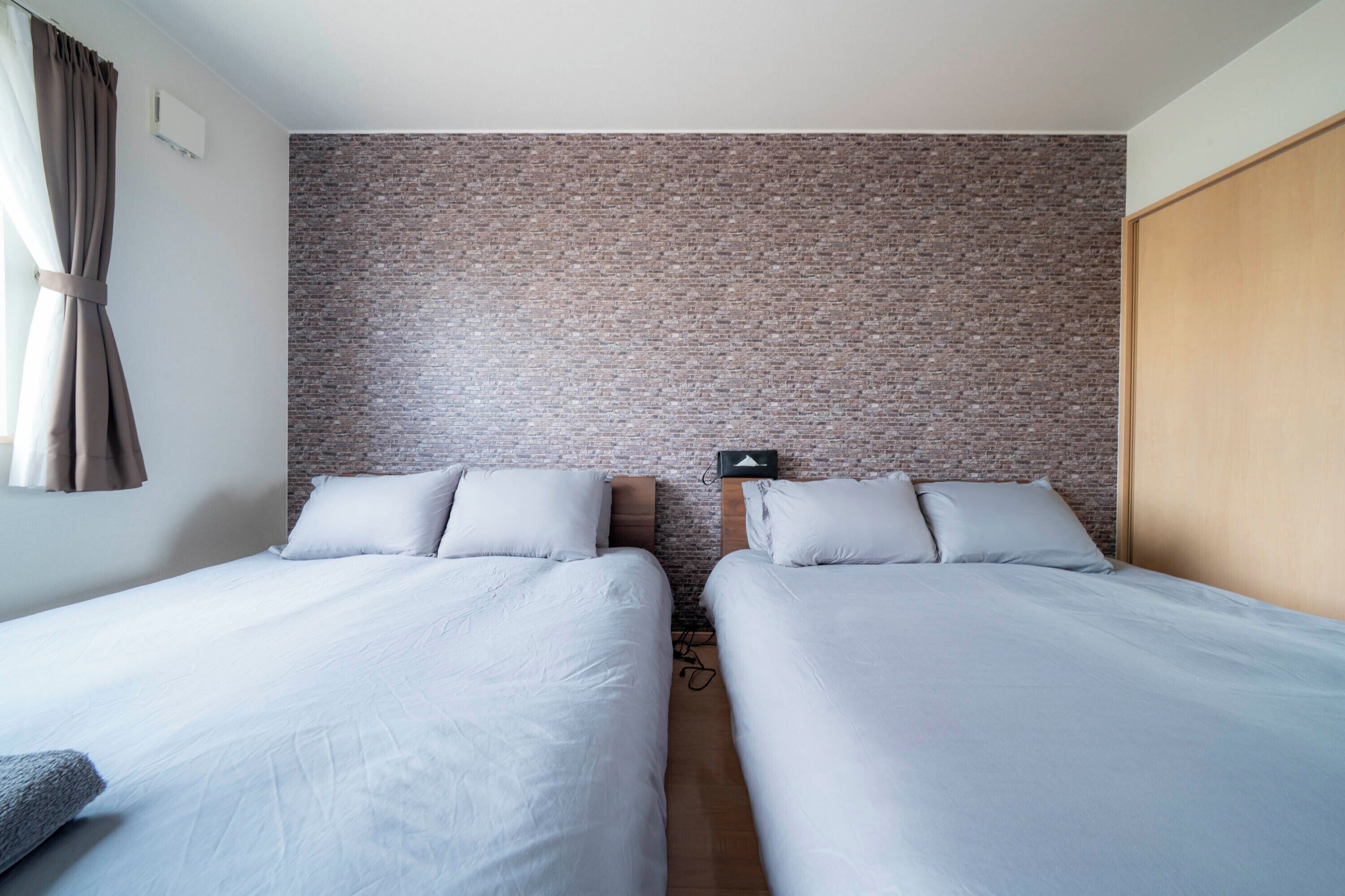 A room with two beds, a brick-patterned wall, a wooden wardrobe, and a power outlet.