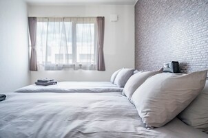 A hotel room with two beds, a brick wall, and a window with sheer curtains.