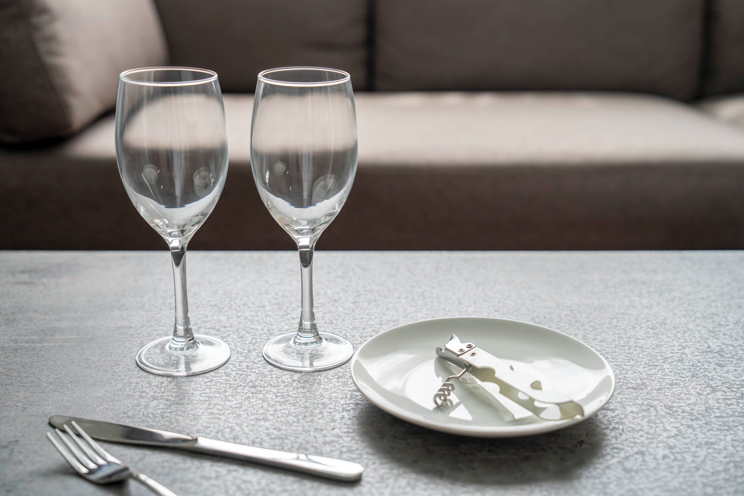 Two empty wine glasses on a table with a fork and a plate with a bottle opener.