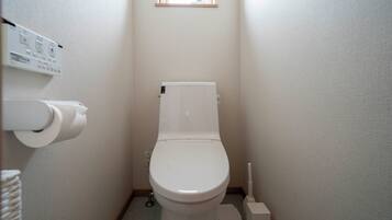 Une petite salle de bain propre, équipée de toilettes, d’un porte-rouleau de papier toilette et d’un bidet.