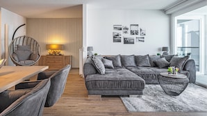 Un salon moderne avec un canapé d’angle, une table à manger et un fauteuil suspendu.