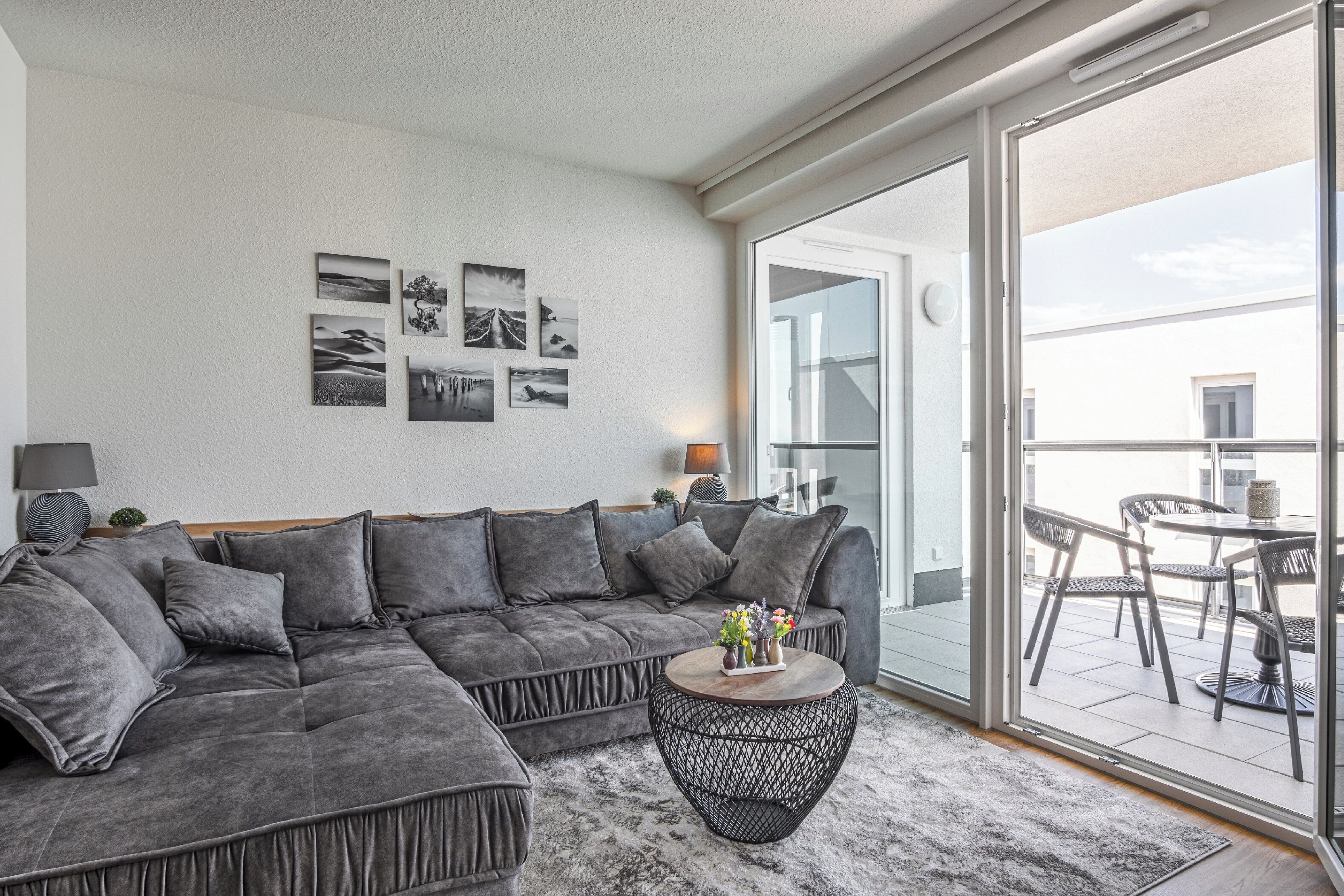 A modern living room with a grey sectional sofa, a round coffee table, and a large sliding glass door leading to an outdoor patio area.