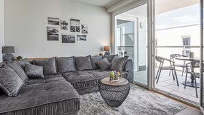 Un salon moderne avec un canapé d’angle gris, une table basse ronde et une grande porte-fenêtre coulissante donnant sur un patio extérieur.
