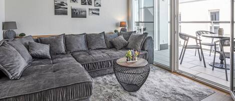 A modern living room with a grey sectional sofa, a round coffee table, and a large sliding glass door leading to an outdoor patio area.