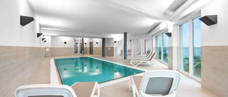 A modern indoor swimming pool with lounge chairs and large windows.