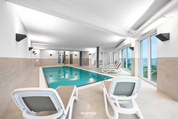A modern indoor swimming pool with lounge chairs and large windows. - Ostseebrise - Indoor swimming pool, sauna, terrace, private parking, by the sea (Olpenitz)