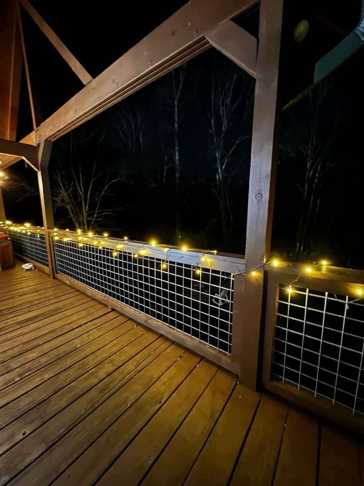 Une terrasse en bois avec une rambarde en métal et des guirlandes lumineuses.
