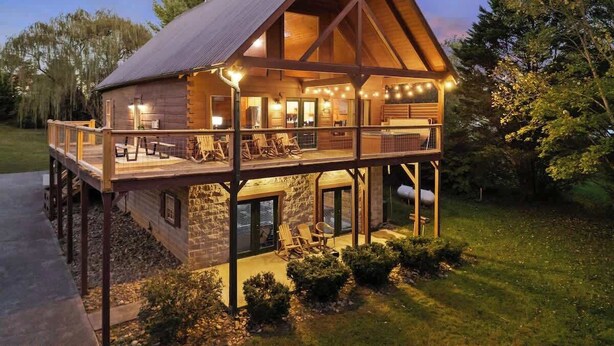 A two-story log cabin with a balcony, stone foundation, and a metal roof.