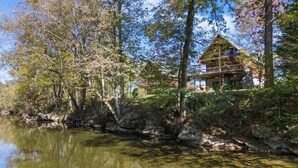 A lakeside cabin with a wooden deck and a large window overlooking the water.