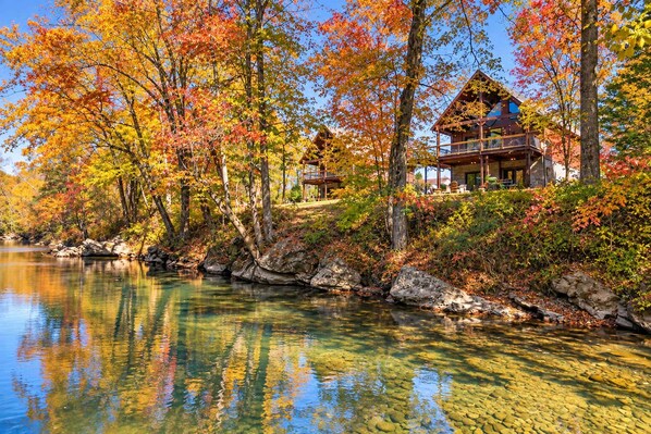 A lakeside cabin with a deck overlooking the water, surrounded by autumn foliage.